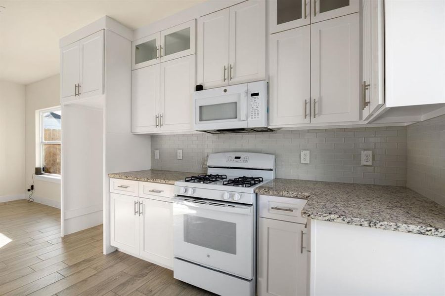 Bright, modern kitchen featuring sleek white cabinets, stunning granite countertops, and brand new appliances. The clean design creates a fresh, inviting space perfect for cooking and entertaining.