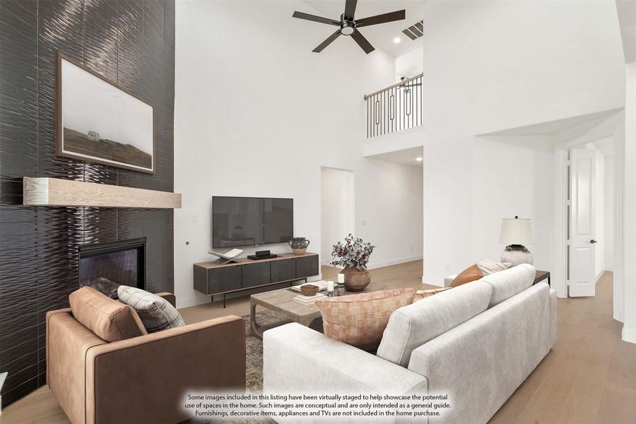Living room with two-story ceiling, dark tile fireplace, ceiling fan, and upper balcony overlook
