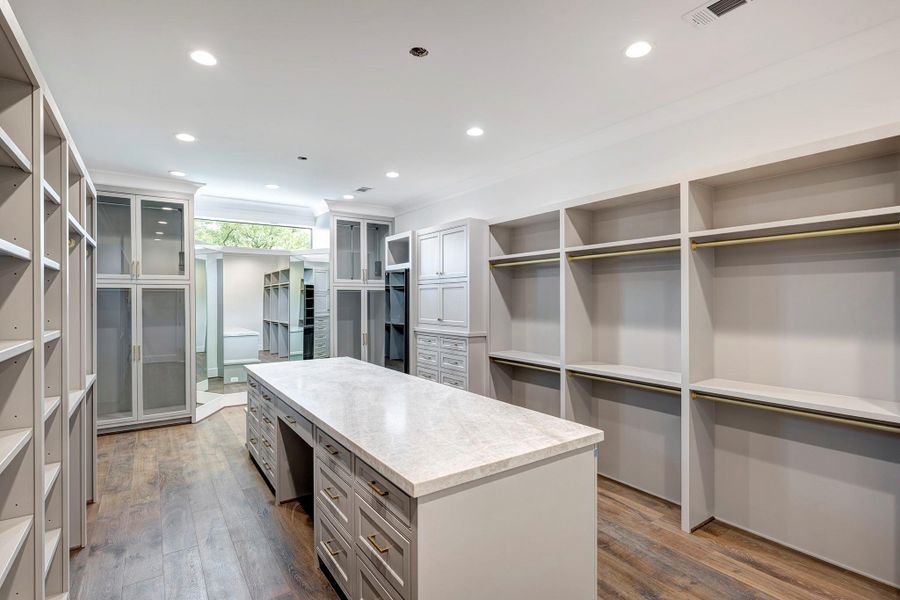 Her closet features a three-way mirror, abundant hanging and drawer space, dedicated shoe storage, and a center island with additional built-in storage. Her closet features a three-way mirror, abundant hanging and drawer space, dedicated shoe storage, and a center island with additional built-in storage.