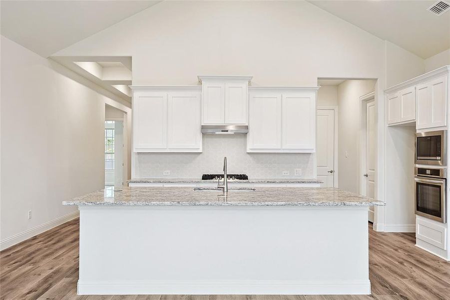 Kitchen with appliances with stainless steel finishes, a center island with sink, white cabinetry, and light hardwood / wood-style flooring