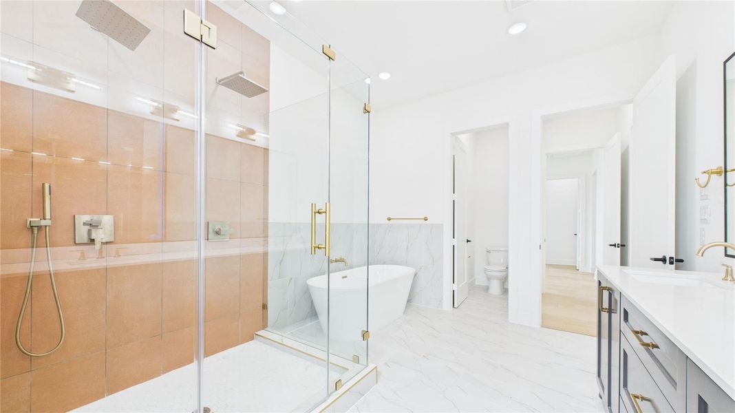 The spacious glass-enclosed shower offers dual rain showerheads, a sleek extra long freestanding bathtub, and elegant fixtures. The room is bright with a clean, minimalist design, offering ample space and a luxurious feel.