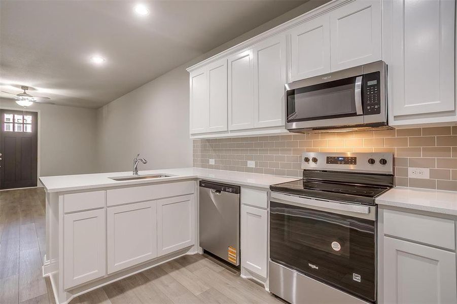 Kitchen with appliances with stainless steel finishes, a peninsula, light wood-style flooring, ceiling fan, and recessed lighting Kitchen with appliances with stainless steel finishes, a peninsula, light wood-style flooring, ceiling fan, and recessed lighting