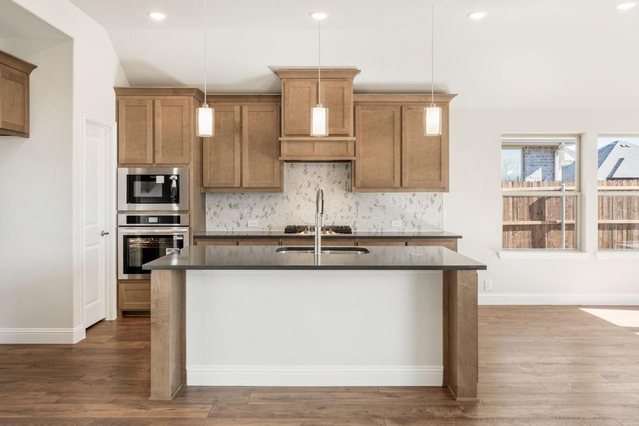 Kitchen with wood cabinets, dark countertop island, pendant lights, and stainless steel double ovens Kitchen with wood cabinets, dark countertop island, pendant lights, and stainless steel double ovens