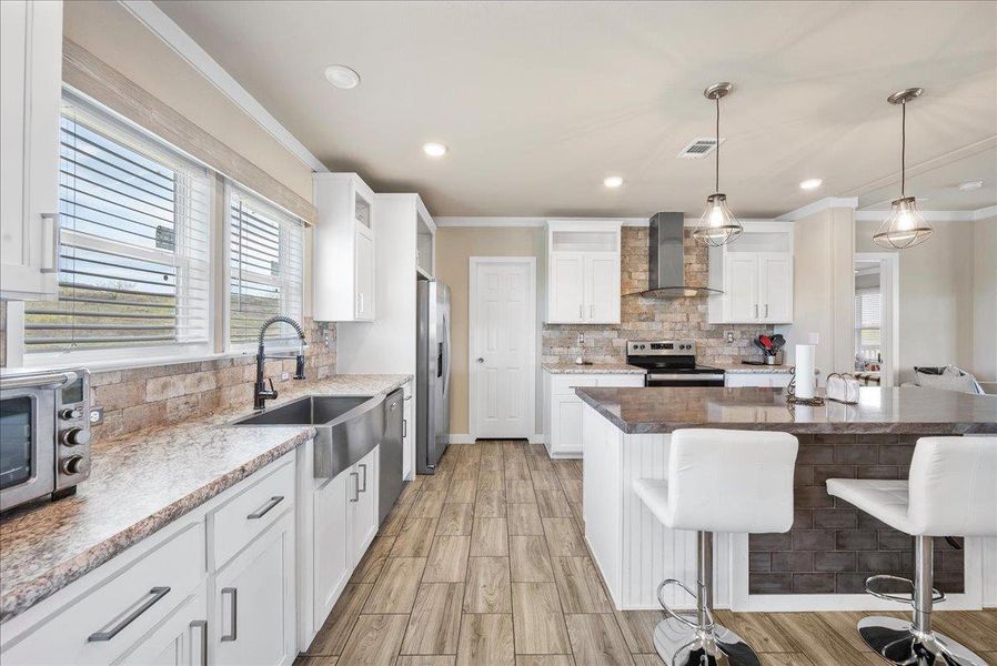 Kitchen with white cabinetry, a breakfast bar area, backsplash, crown molding, and stainless steel appliances Kitchen with white cabinetry, a breakfast bar area, backsplash, crown molding, and stainless steel appliances