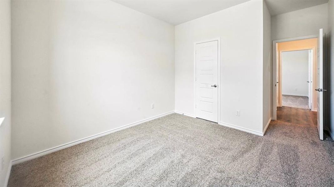 Spacious room featuring light gray carpet, crisp white walls, and a five-panel interior door with brushed nickel hardware