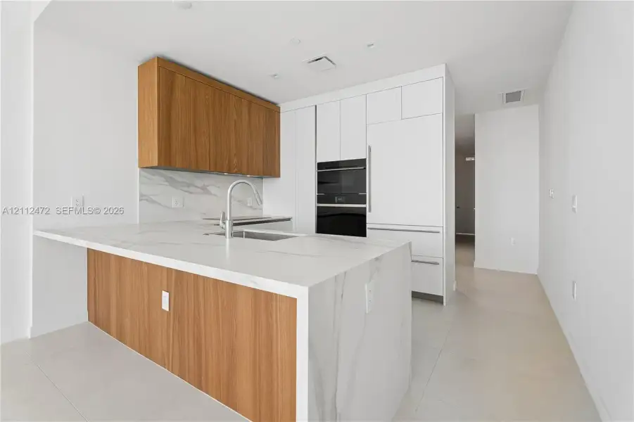 Kitchen featuring a waterfall-edge island with stone-finish countertop, wood-finish cabinetry, built-in wall oven and microwave, panel-ready refrigerator, and stone-finish backsplash