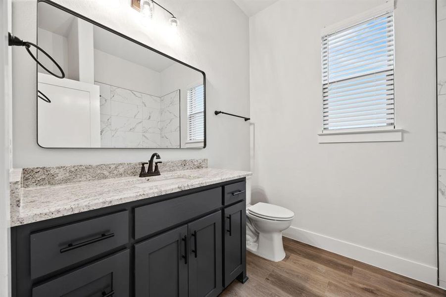 Full bath featuring plenty of natural light, baseboards, wood finished floors, and vanity