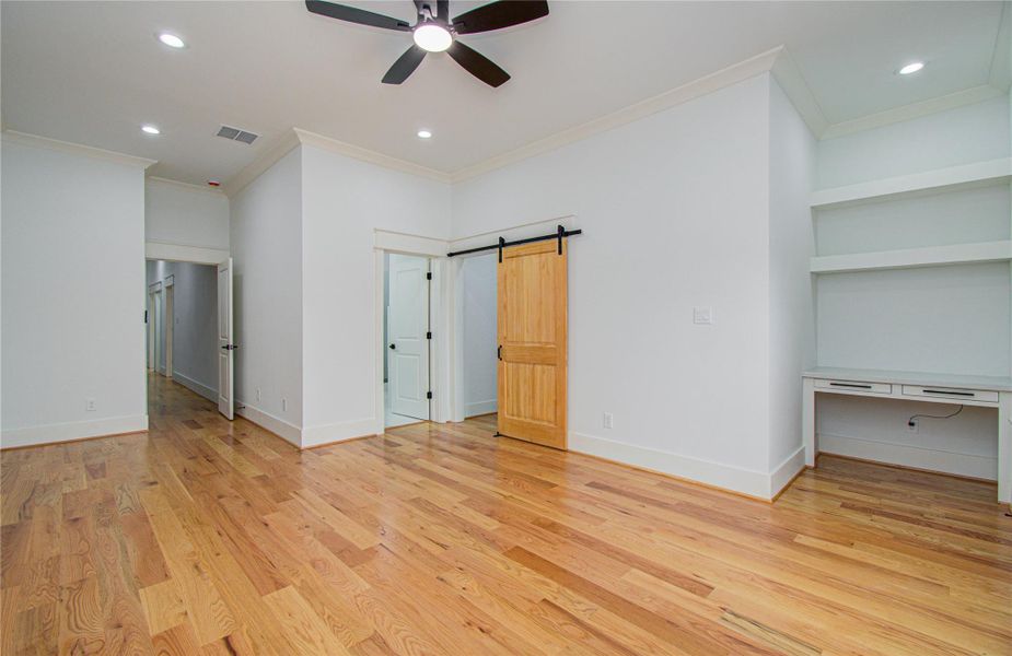 This spacious primary bedroom features beautiful hardwood floors, a ceiling fan, and a modern barn door. It includes built-in shelves and a desk area, making it ideal for a private home office or study.