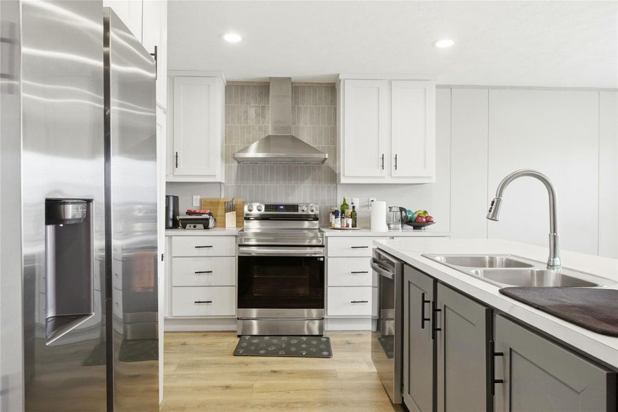 A well-equipped kitchen features light wood flooring, white cabinetry, and stainless steel appliances, all illuminated by recessed lighting.
