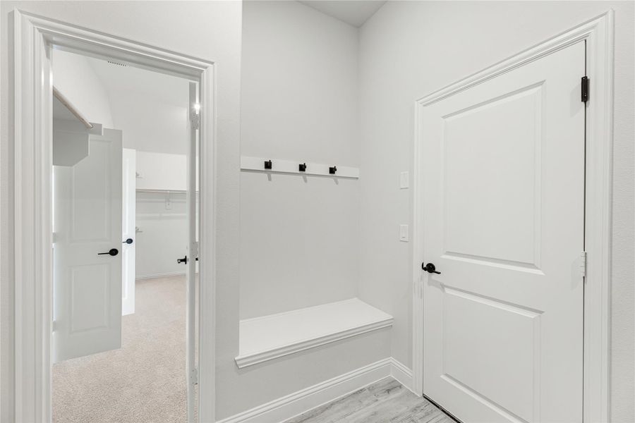 Mudroom with built-in bench, wall hooks, and white doors leading to carpeted hallway