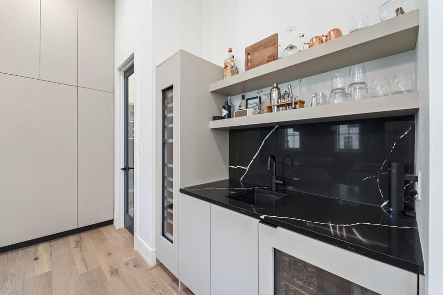 This modern wet bar is highlighted by sleek cabinetry, open shelving, and a striking black marble countertop. With a sink, wine fridge, beverage fridge, and ample storage, it offers a stylish and functional space perfect for entertaining. This modern wet bar is highlighted by sleek cabinetry, open shelving, and a striking black marble countertop. With a sink, wine fridge, beverage fridge, and ample storage, it offers a stylish and functional space perfect for entertaining.