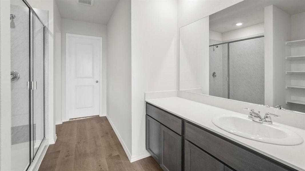 Bathroom featuring a vanity with a white countertop and an integrated sink, a large mirror, a shower with a clear glass enclosure, and wood-look flooring
