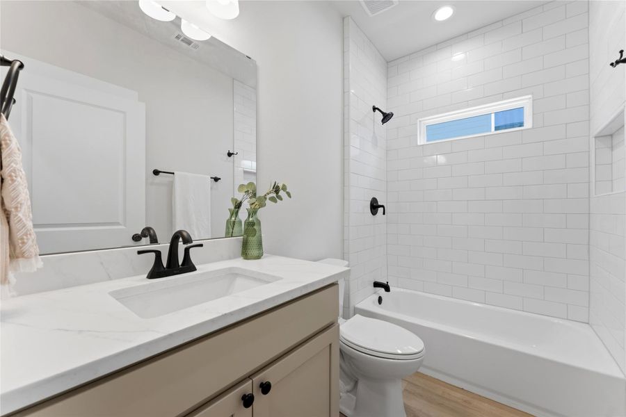 Warm, organic finishes include oat-colored cabinetry, marble-look countertops, and a tiled tub and shower combination. Conveniently located in a hall between the two secondary bedrooms for easy access by family and guests.