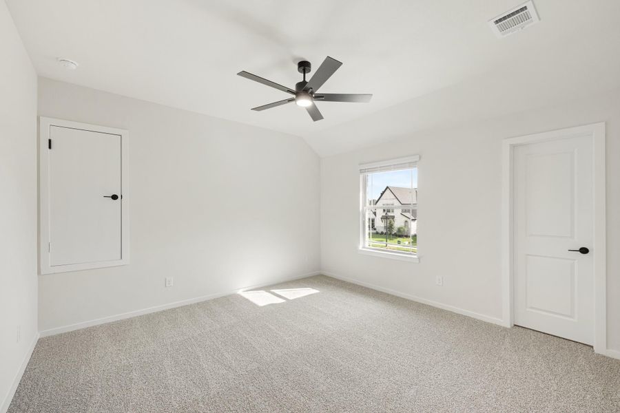 Empty bedroom with vaulted ceiling, ceiling fan, carpet flooring, and two white doors
