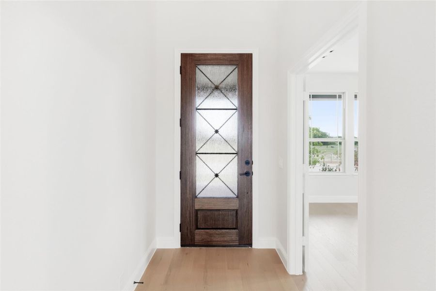 Entryway with dark wood front door featuring decorative glass panels and light hardwood floors Entryway with dark wood front door featuring decorative glass panels and light hardwood floors