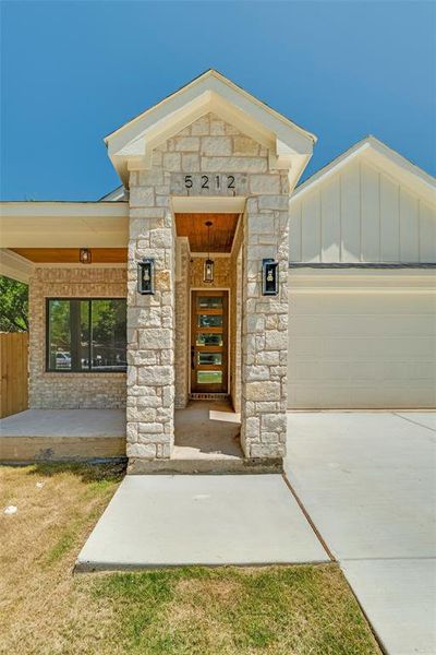 Entrance to property featuring stone siding, a garage, and concrete driveway