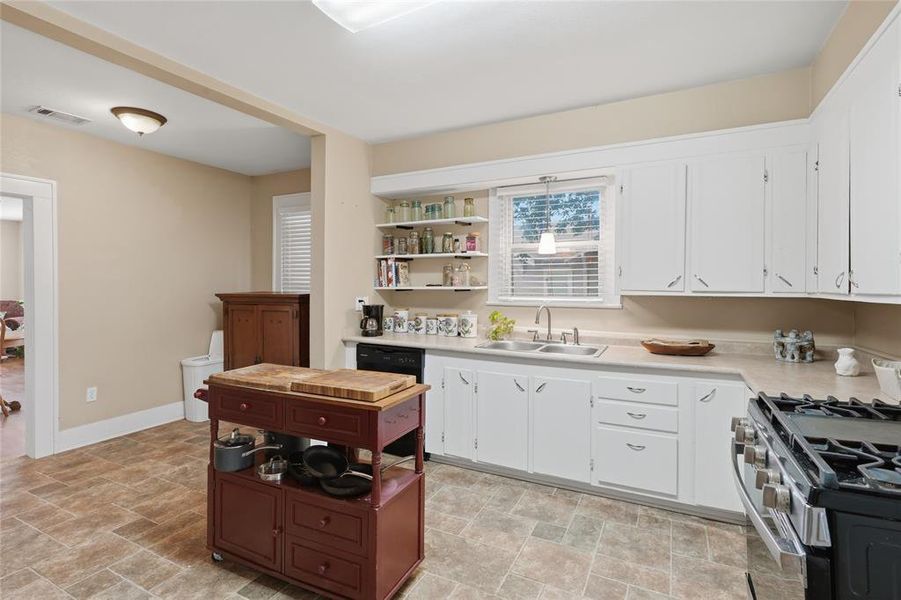 Kitchen featuring white cabinetry, a double basin stainless steel sink, a gas range, and open shelving