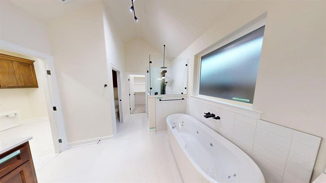 Bathroom with a jetted tub, walk in shower, vaulted ceiling, vanity, and tile walls