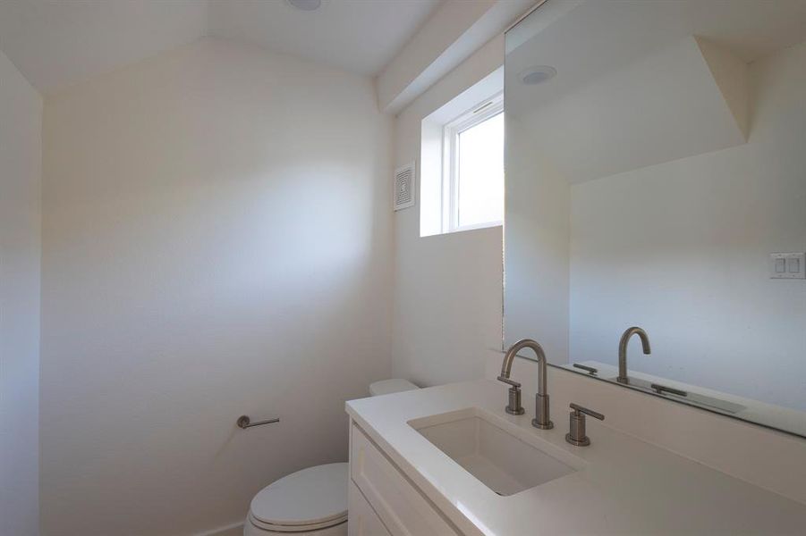 Half bathroom featuring lofted ceiling, visible vents, toilet, and vanity