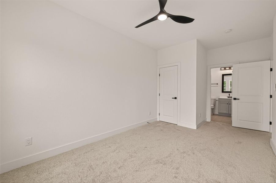 This bright bedroom features neutral walls and carpet, a modern ceiling fan, a closet, and an en-suite bathroom with sleek fixtures. This bright bedroom features neutral walls and carpet, a modern ceiling fan, a closet, and an en-suite bathroom with sleek fixtures.