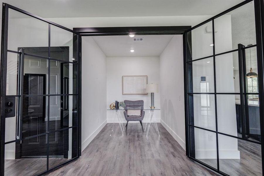 Entryway featuring black-framed glass French doors opening to a room with wood-finish flooring, recessed lighting, and white baseboards Entryway featuring black-framed glass French doors opening to a room with wood-finish flooring, recessed lighting, and white baseboards