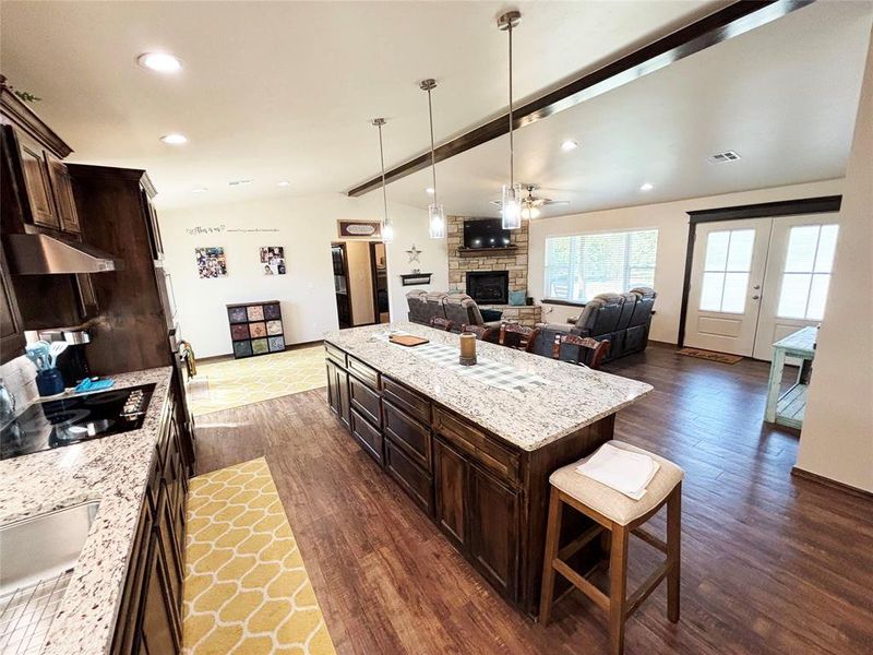 Kitchen featuring dark brown cabinets, light stone countertops, a stone fireplace, a kitchen breakfast bar, and decorative light fixtures Kitchen featuring dark brown cabinets, light stone countertops, a stone fireplace, a kitchen breakfast bar, and decorative light fixtures