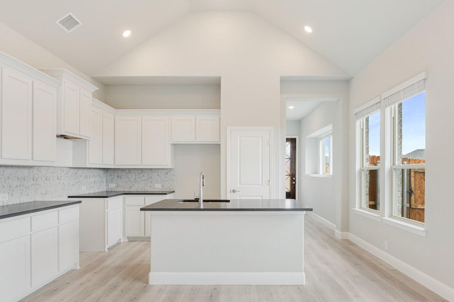 Kitchen with white cabinets, dark countertops, center island, tile backsplash, and vaulted ceiling