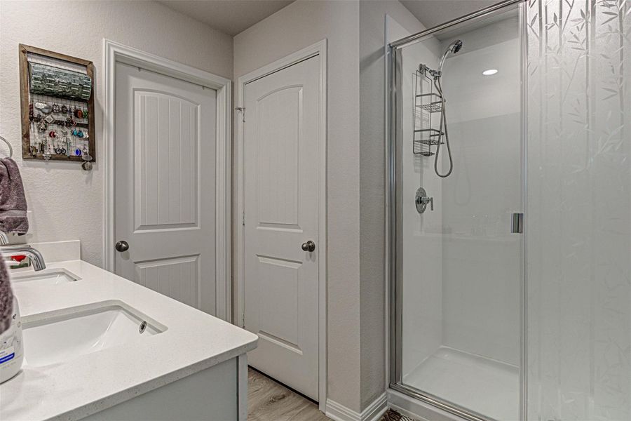 Bathroom featuring a shower stall, double vanity, light wood finished floors, and a textured wall