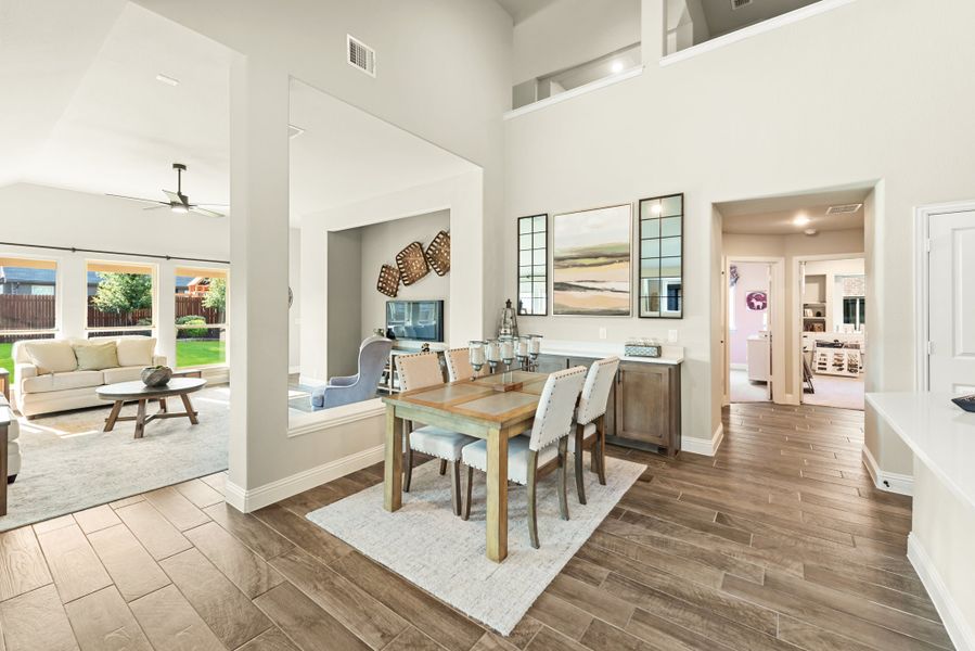 Open-concept dining area with high ceilings, wood-look floors, and view into living room