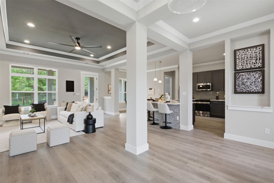 An open concept living area boasts elegant tray ceilings and durable hardwood-style flooring, connecting seamlessly to a modern kitchen. An open concept living area boasts elegant tray ceilings and durable hardwood-style flooring, connecting seamlessly to a modern kitchen.
