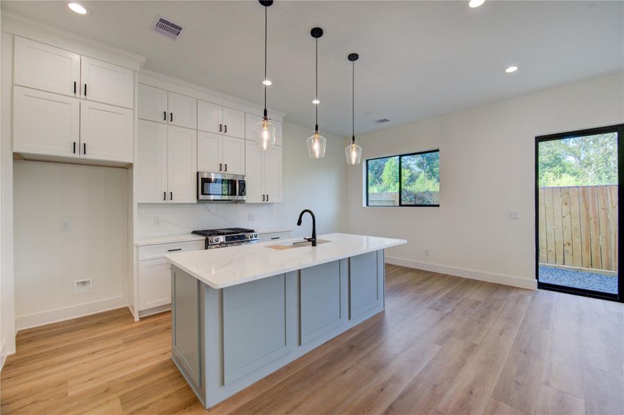 This modern kitchen features sleek white cabinetry, a center island, and stylish pendant lighting. It has stainless steel appliances, a large window for natural light, and an open layout with vinyl plank flooring, creating a bright and inviting space. This modern kitchen features sleek white cabinetry, a center island, and stylish pendant lighting. It has stainless steel appliances, a large window for natural light, and an open layout with vinyl plank flooring, creating a bright and inviting space.