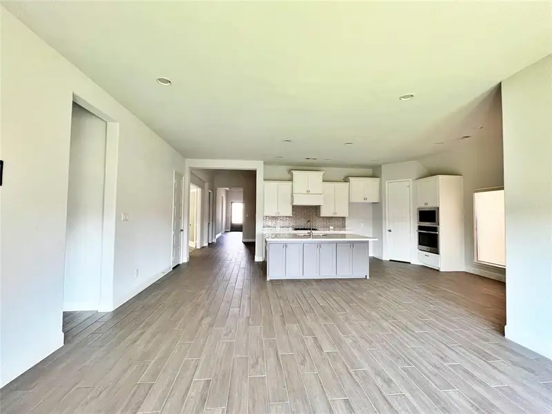 Kitchen with tasteful backsplash, white cabinets, light wood-type flooring, a center island with sink, and oven Kitchen with tasteful backsplash, white cabinets, light wood-type flooring, a center island with sink, and oven