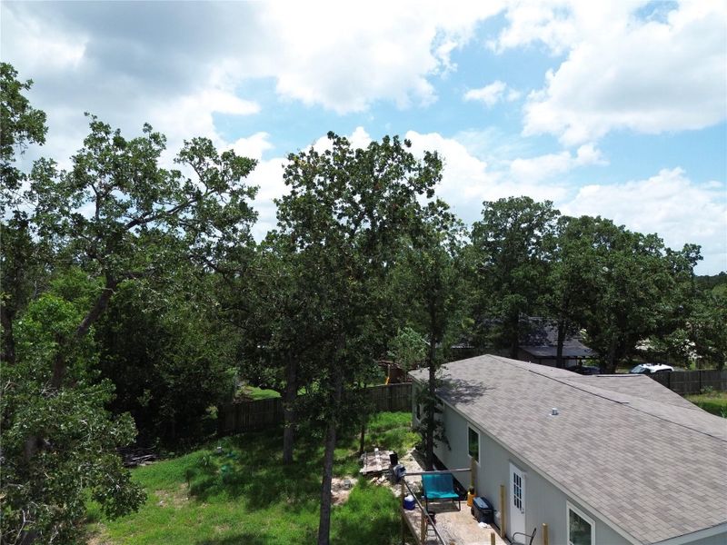 An aerial perspective reveals a private yard surrounded by a lush tree canopy and a comfortable outdoor deck.