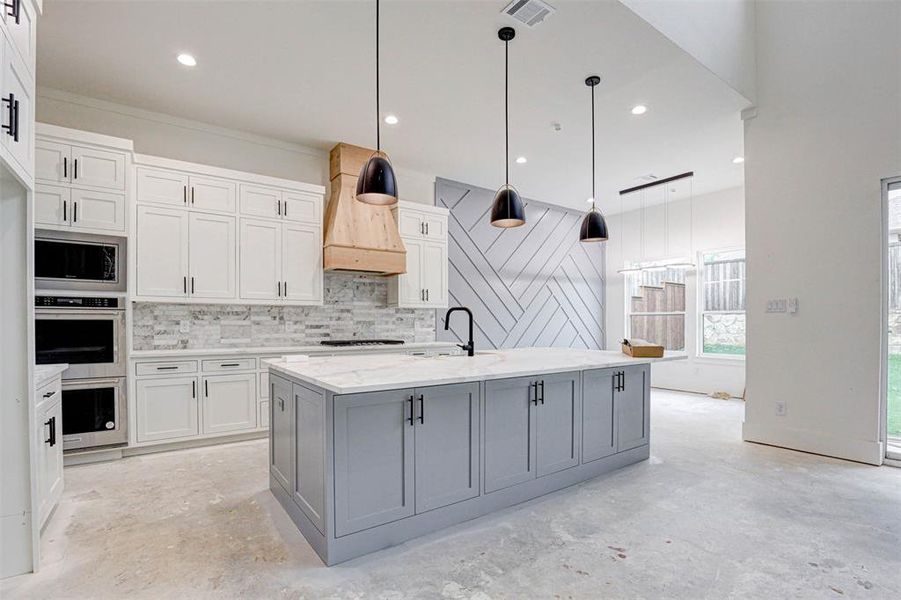 Kitchen featuring premium range hood, gray cabinetry, pendant lighting, white cabinetry, and an island with sink