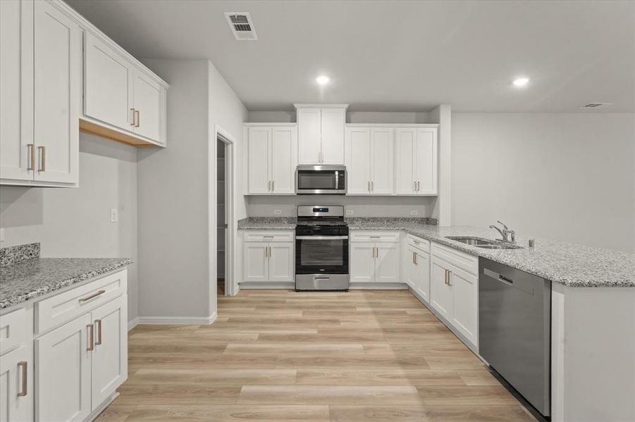 Kitchen with light stone countertops, appliances with stainless steel finishes, white cabinetry, light hardwood / wood-style floors, and sink