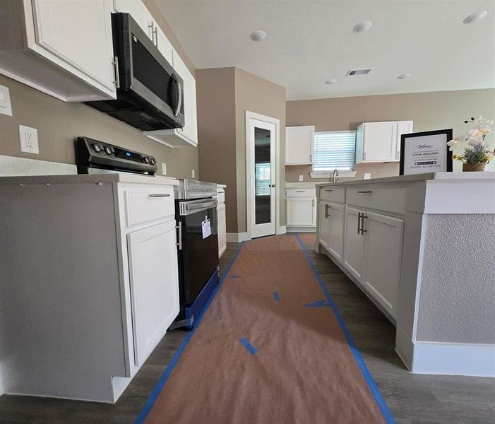 Kitchen with appliances with stainless steel finishes, dark wood-style floors, white cabinetry, a sink, and light countertops Kitchen with appliances with stainless steel finishes, dark wood-style floors, white cabinetry, a sink, and light countertops