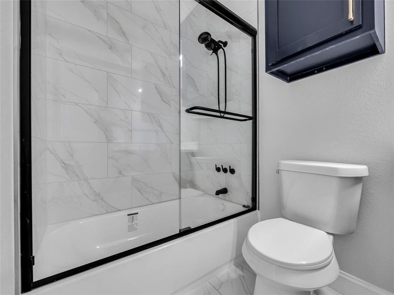 Bathroom with combined bath / shower with glass door and marble finish floors Bathroom with combined bath / shower with glass door and marble finish floors