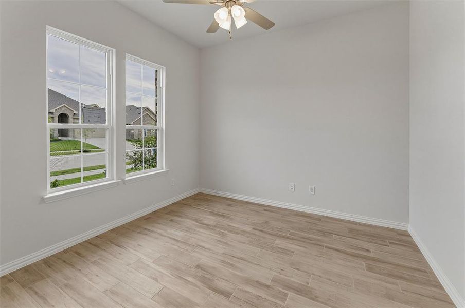 Bright room featuring two large windows, wood-finish flooring, a ceiling fan, and crisp white baseboards