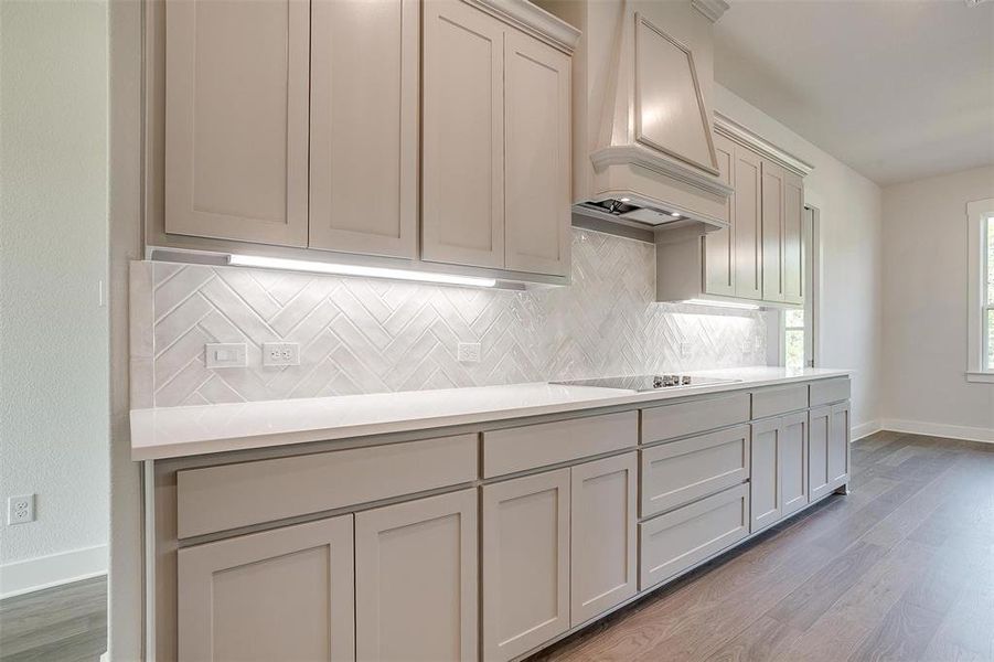 Kitchen featuring hardwood / wood-style flooring, decorative backsplash, premium range hood, and stovetop