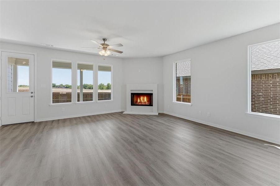 Spacious living area featuring wood-finish flooring, a corner fireplace, multiple windows, a ceiling fan, and a glass-paneled exterior door