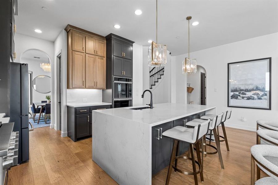 Kitchen featuring arched walkways, a chandelier, light stone counters, dark cabinets, and recessed lighting Kitchen featuring arched walkways, a chandelier, light stone counters, dark cabinets, and recessed lighting