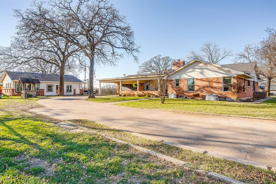 Ranch-style house featuring concrete driveway, a chimney, brick siding, a front lawn, and covered porch