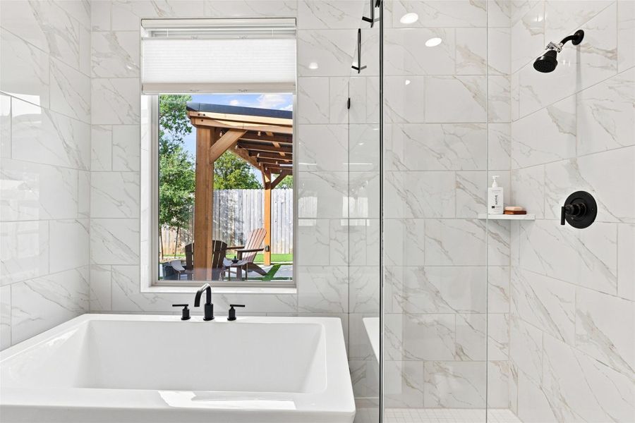 Floor-to-ceiling marble-look tile surrounds a deep soaking tub and glass-enclosed shower.