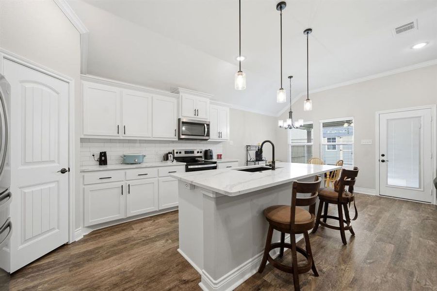 Kitchen featuring a kitchen bar, vaulted ceiling, stainless steel appliances, white cabinetry, and dark wood-type flooring