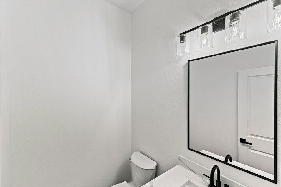 This photo shows the half bathroom with a sleek black-framed mirror, elegant light fixtures, and a white vanity with a black faucet. The space is bright and minimalistic. This photo shows the half bathroom with a sleek black-framed mirror, elegant light fixtures, and a white vanity with a black faucet. The space is bright and minimalistic.