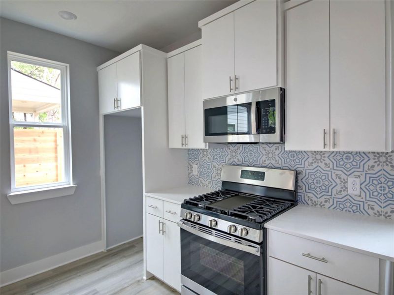 Kitchen with appliances with stainless steel finishes, white cabinets, tasteful backsplash, and light wood-type flooring