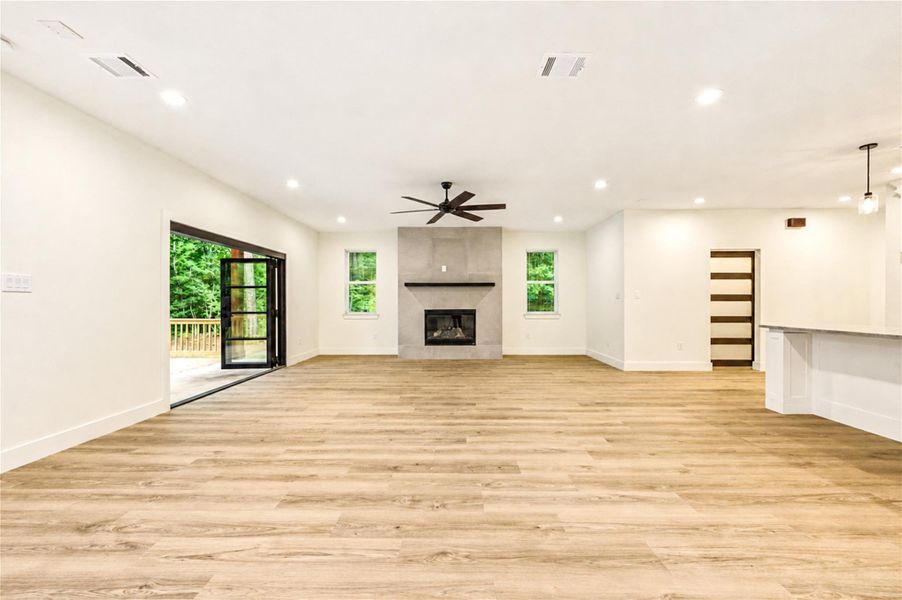 Spacious open-concept living area with beautiful wood flooring, a modern gas fireplace, and large folding doors leading to a serene outdoor deck.