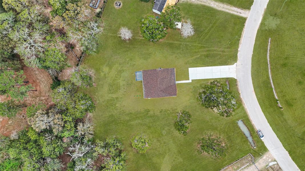 This aerial photo shows a single-story home with a brown roof, nestled in a spacious, grassy area surrounded by trees. A long driveway leads to the house, and there's a curved road nearby. The setting is private and serene, offering plenty of open space. This aerial photo shows a single-story home with a brown roof, nestled in a spacious, grassy area surrounded by trees. A long driveway leads to the house, and there's a curved road nearby. The setting is private and serene, offering plenty of open space.