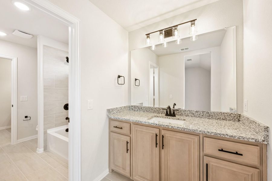 Bathroom with wood vanity, granite countertop, large mirror, and soaking tub visible in background Bathroom with wood vanity, granite countertop, large mirror, and soaking tub visible in background