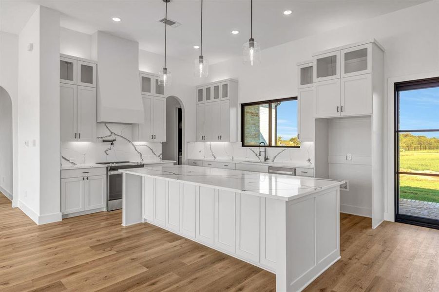 Kitchen with glass insert cabinets, light stone counters, tasteful backsplash, arched walkways, and stainless steel electric range oven